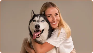 Femme souriante en train de câliner un husky noir et blanc avec les yeux bleus, illustrant une relation de confiance avec son chien