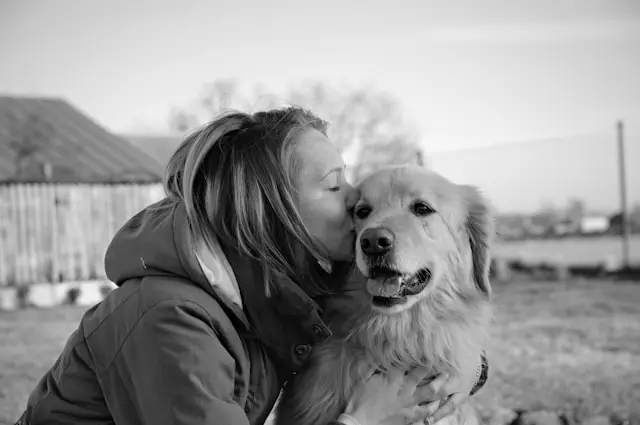 Une femme embrasse tendrement un golden retriever en extérieur, sur une photo en noir et blanc.