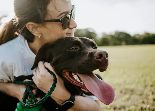Une femme souriante enlace un chien marron, tous deux profitant d’un moment de complicité en extérieur.