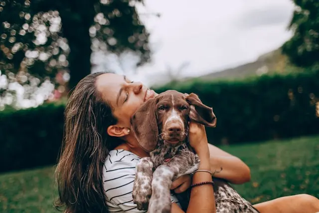 Une femme enlace tendrement son chien dans un jardin, profitant d’un moment de complicité à l’extérieur.